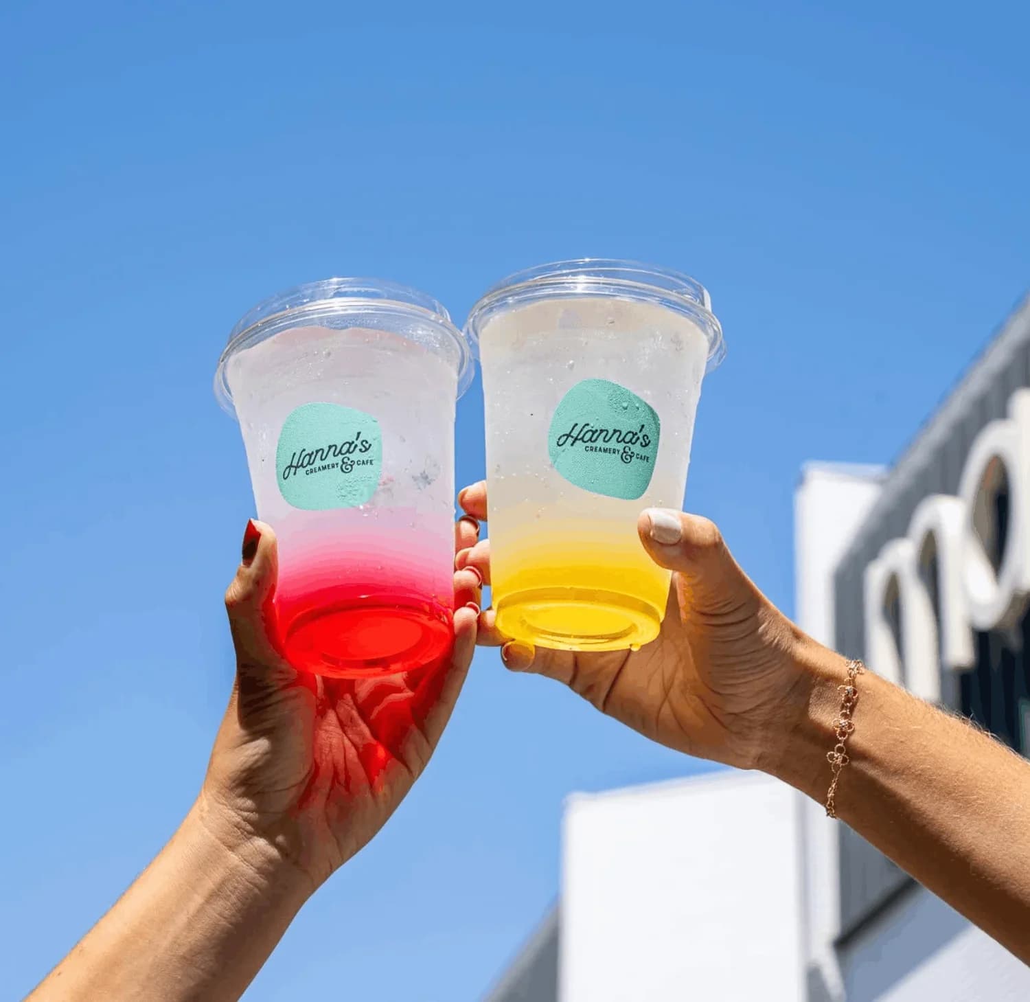 Two colorful Hanna’s drinks raised in the sunshine
